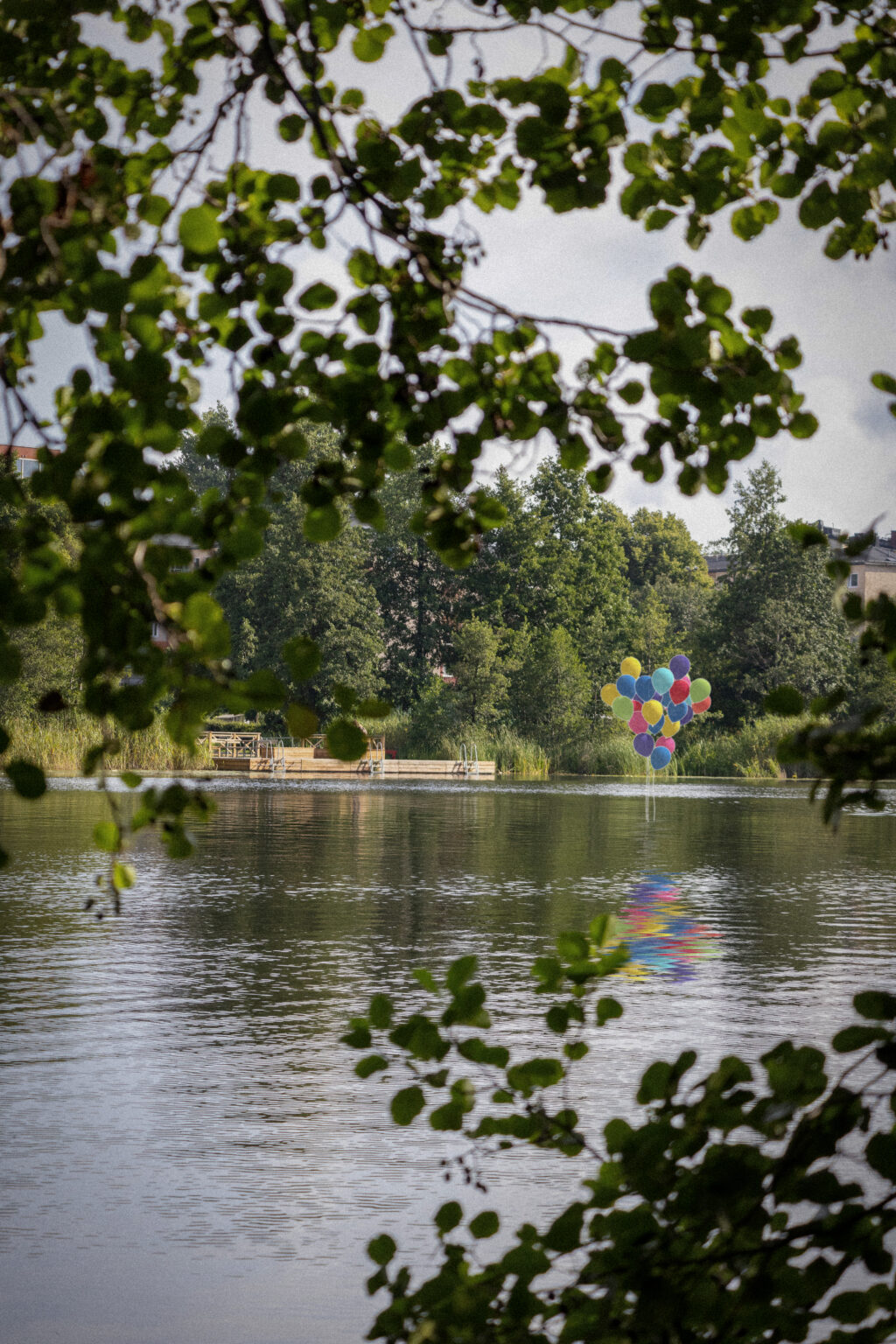 Skiss för verket To the Moon by Balloon. Färgglada ballonger stiger upp ur Sicklasjön, brygga i bakgrunden.